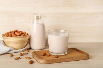 Board with glass of healthy almond milk and nuts on wooden background