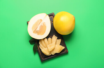 Wooden board with whole pomelo fruit and slices on green background