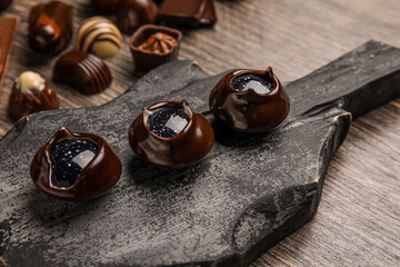 Dark board with chocolate candies on wooden table, closeup