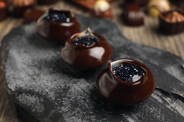Dark board with chocolate candies on wooden table, closeup
