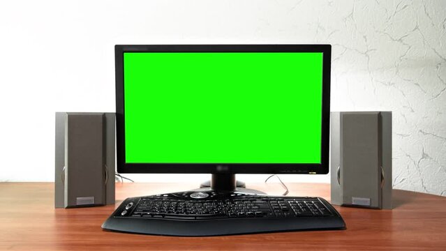 Computer green screen monitor is standing on a desk in an office timelapse hyperlapse forward motion. Design of workplace with grey audio speakers and black keyboard