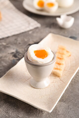 Holder with soft boiled egg and toasted bread on grey table