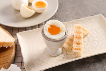 Holder with soft boiled egg and toasted bread on grey table