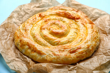 Delicious cheese pie in baking paper on blue background