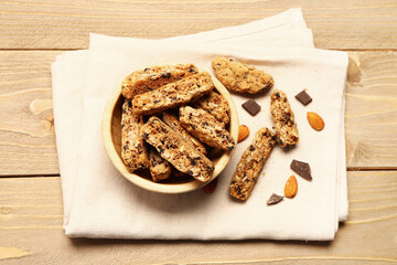Napkin with bowl of tasty biscotti cookies, almond nuts and chocolate on wooden background