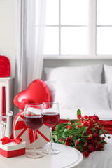 Glasses of wine, candle and gifts for Valentine's Day on table in bedroom, closeup