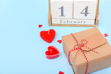 Cube calendar with date 14 FEBRUARY, gift and candles on blue background, closeup