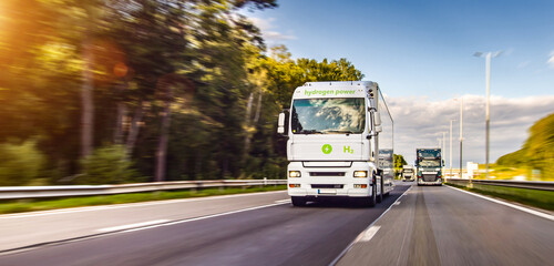 Hydrogen powered H2 Cargo semi truck driving on a highway. White Truck delivers goods in early hours of the Morning - very low angle drive thru close up shot -  motion blur effect - 558234137