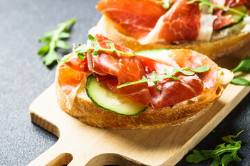 Open sandwiches with cream cheese, prosciutto, cucumber and arugula at wooden table.