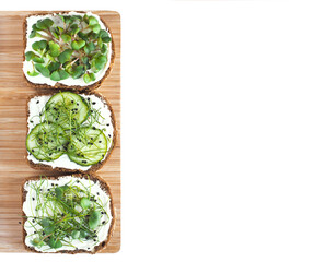 Close-up banner with healthy food isolated on white background.  Three different toasts on whole grain bread with home grown microgreens and cucumber on cream cheese. Copy space.