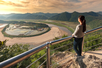 Fototapeta na wymiar HOERYONGPO, SOUTH KOREA – June 2010: young Korean woman observing sunrise over the meander, the countryside and the mountains, North Gyeongsang Province