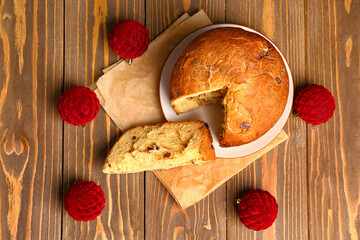 Plate with cut Panettone and Christmas balls on wooden background