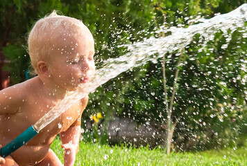 Child toddler boy playing with water hose outdoors in summer, summer activities 