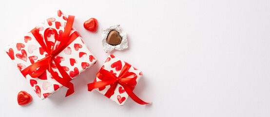 Valentine's Day concept. Top view photo of present boxes with red ribbon bows and heart shaped chocolate candies on isolated white background with copyspace