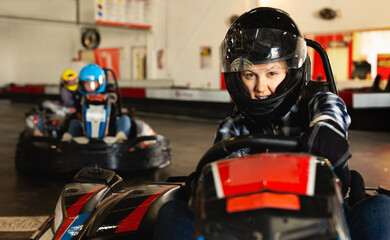 Portrait of female racer in helmet driving the kart on track