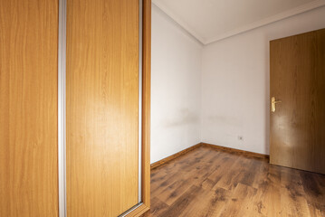 Empty room with built-in wardrobe with aluminum-edged oak sliding doors and dark wooden flooring