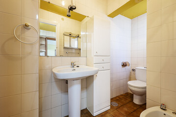 Old bathroom with a lacquered wooden column cabinet, a rectangular frameless mirror, dark stoneware floors and cream-colored tiled walls