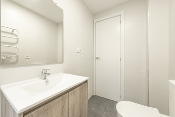 Fototapeta na wymiar Small bathroom with newly installed modern cabinets, frameless mirror and smooth light gray tiles
