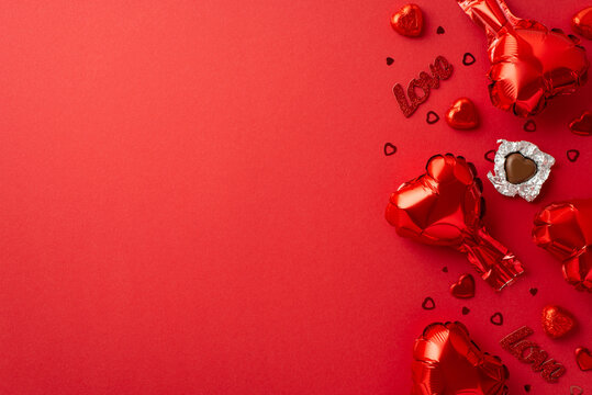 St Valentine's Day concept. Top view photo of heart shaped balloons unwrapped chocolate candies inscription love and confetti on isolated red background with empty space