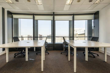 Twin white office desks with black swivel chairs and large windows overlooking the city