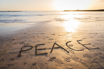 "Peace" written on the sand at the beach during sunset, photo with copy space.