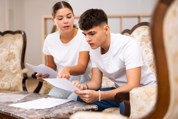 Young man signing documents under close attention of woman