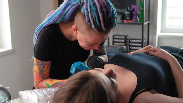 Tattoo artist girl at work.A feminist with dreadlocks gets a tattoo.A strong woman gets a tattoo.Close-up.Slow motion.The master fills a beautiful abstract tattoo. Concept of gender expression. LGBTQ+