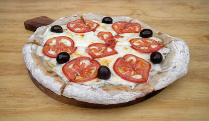 Closeup view of a traditional italian with mozzarella cheese, tomato, garlic, onion and black olives, on the wooden table.