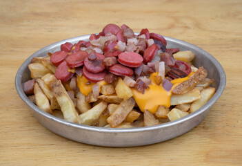 Fries. Closeup view of fried potatoes with sliced sausages and crispy bacon, in a metal dish with a wooden background.
