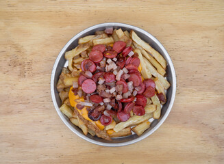 Fries. Top view of fried potatoes with sliced sausages and crispy bacon, in a metal dish with a wooden background.