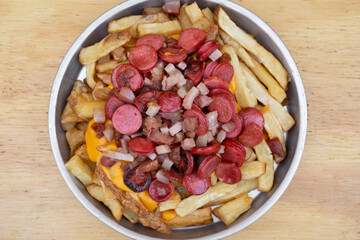 Fries. Top view of fried potatoes with sliced sausages and crispy bacon, in a metal dish with a wooden background.