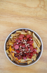 Fries. Top view of fried potatoes with sliced sausages and crispy bacon, in a metal dish with a wooden background.