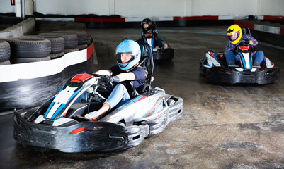 Group of glad cheerful positive people driving go-carts at racing track