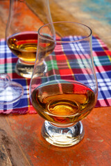 Tulip-shaped tasting glass with dram of Scotch single malt or blended whisky on wooden table with tartan
