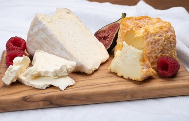 Board with french soft cheeses, Delice de Bourgogne French cow's milk cheese from Burgundy region of France and yellow langres cheese served with fresh raspberries