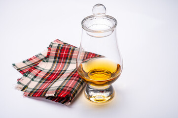 Tulip-shaped tasting glass with dram of Scotch single malt or blended whisky on white background with tartan