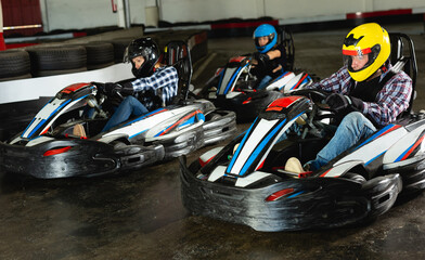 Young positive people in helmets driving racing cars for karting in sport club