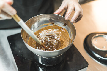 Melting chocolate in a metal bowl. High angle view. Closeup shot. Baker or chef whisking melted chocolate in a bowl with spatula. High quality photo