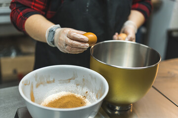 A expert breaking an egg on a metal bowl. Grey, plastic bowl with mixture inside placed next to the metal bowl. High quality photo