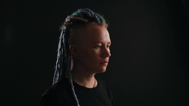 a serious girl with multicolored dreadlocks stands on a black background. Gay girl. Concept of gender expression, identity and diversity. gender person. Feminism