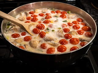 Pan of boiling coconut milk soup with mushrooms and tomatoes with wooden spoon.