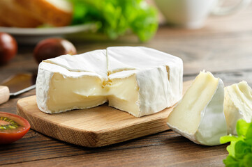 Gourmet  camembert cheese on a cutting board. Tomatoes and lettuce salad on background.