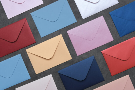 Rows of envelopes of different colors on gray background. Top view, flat lay.