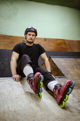 Young athletic roller skater looking at camera while sitting on ramp 