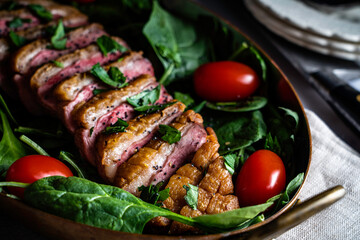 Pan-roasted duck breast served with spinach, arugula, and grape tomatoes. Garnished with parsley and black poppy seeds.