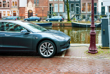 AMSTERDAM, NETHERLANDS, electric car charging at a plug-in charging station on the street by a canal in Amsterdam