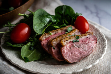 Pan-roasted duck breast served with spinach, arugula, and grape tomatoes. Garnished with parsley and black poppy seeds.