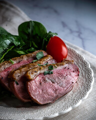 Pan-roasted duck breast served with spinach, arugula, and grape tomatoes. Garnished with parsley and black poppy seeds.