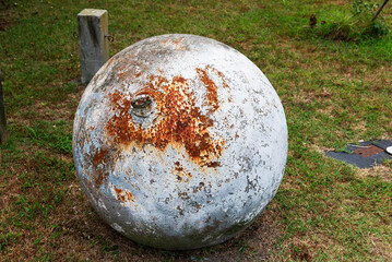 massive rusted iron ball. An industrial anchor with oxides and rust lies on the grass.