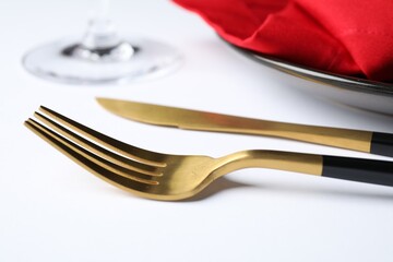 Golden cutlery near plate on white table, closeup